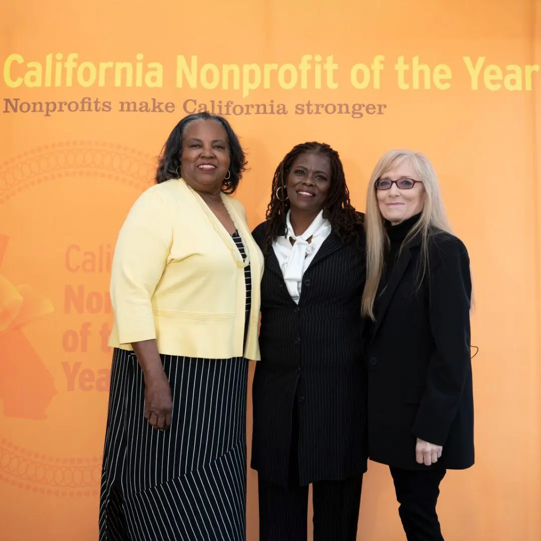 Three women awardees of the 2019 California Nonprofit of the Year stand in front of the orange event banner