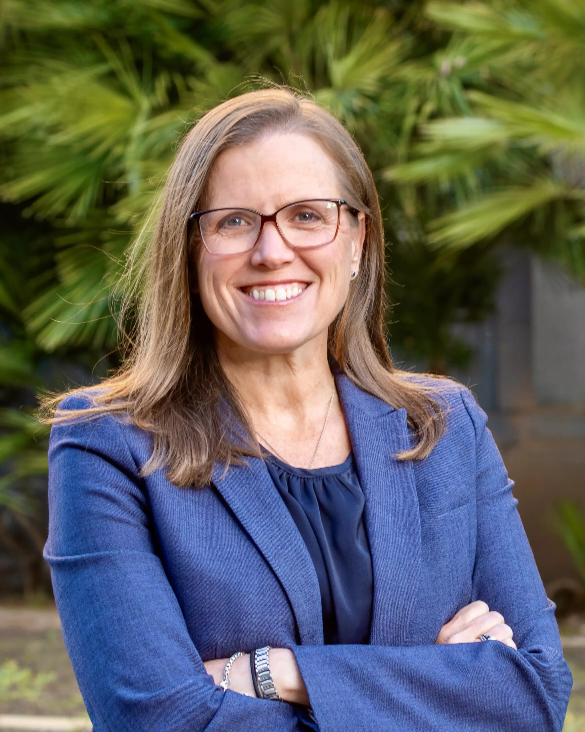 A white woman, Jennifer Fearing, with shoulder length brown hair, glasses, wearing a blue suit. Hands crossed.