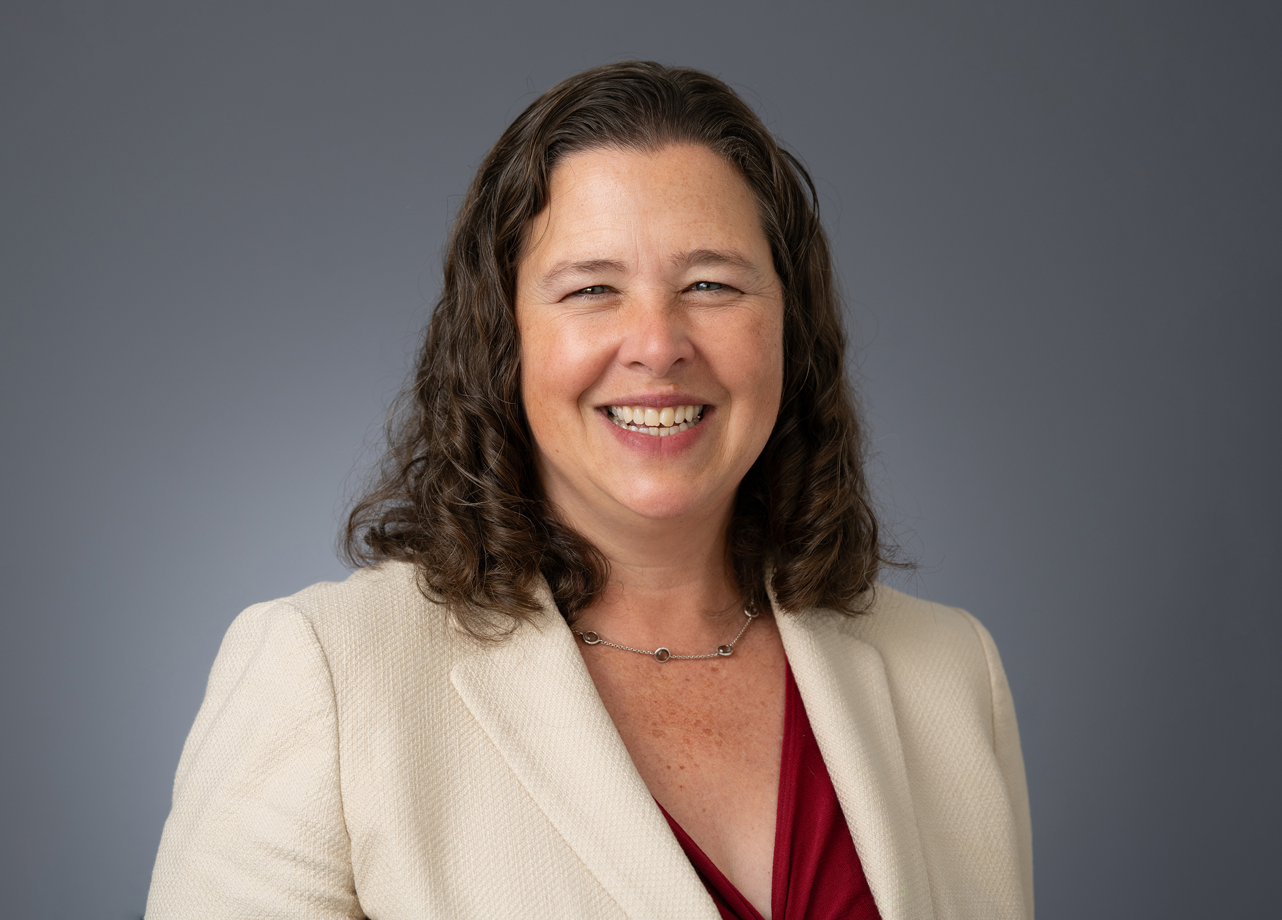 Kate Gordon, headshot, woman, shoulder length brown hair, cream jacket, smiling. Light skin.