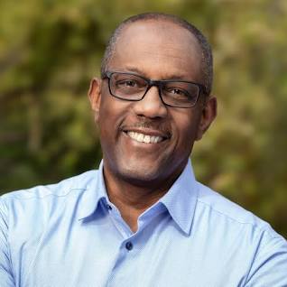 headshot, Chet Hewitt, smiling middle-aged man in a light blue shirt, glasses, African American